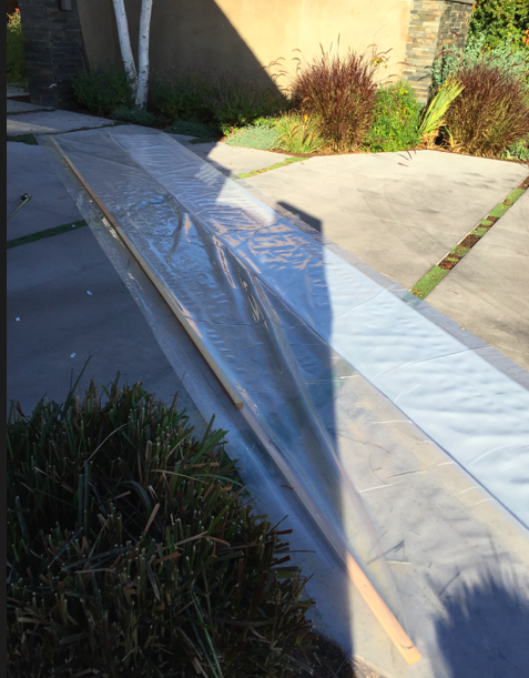 Laying the plastic film on the driveway and fastening the wood strips to the ends.
